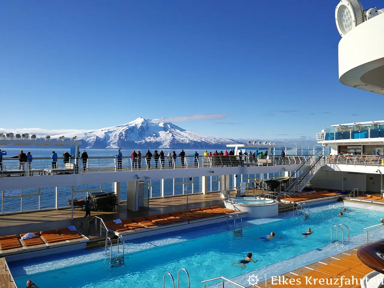 Pooldeck eines Kreuzfahrtschiffs, im Hintergrund schneebedeckte Berge